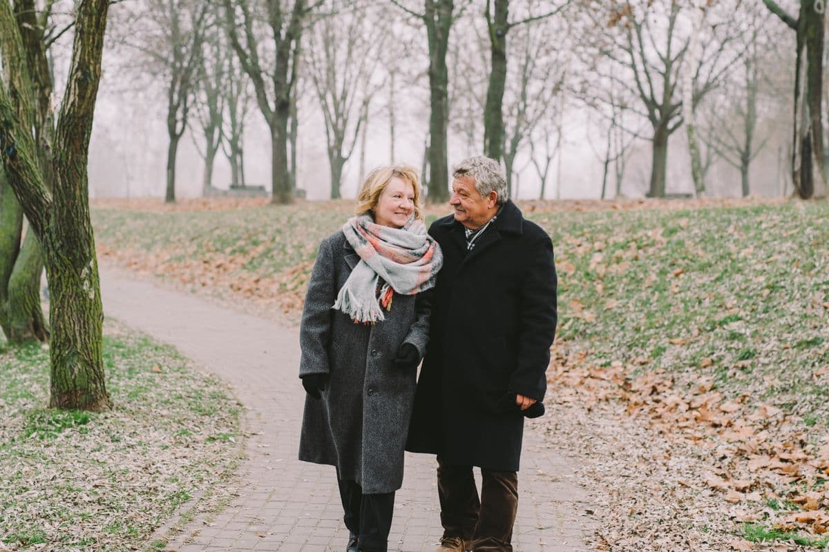 Ouder koppel wandelt pratend over een pad tussen de bomen